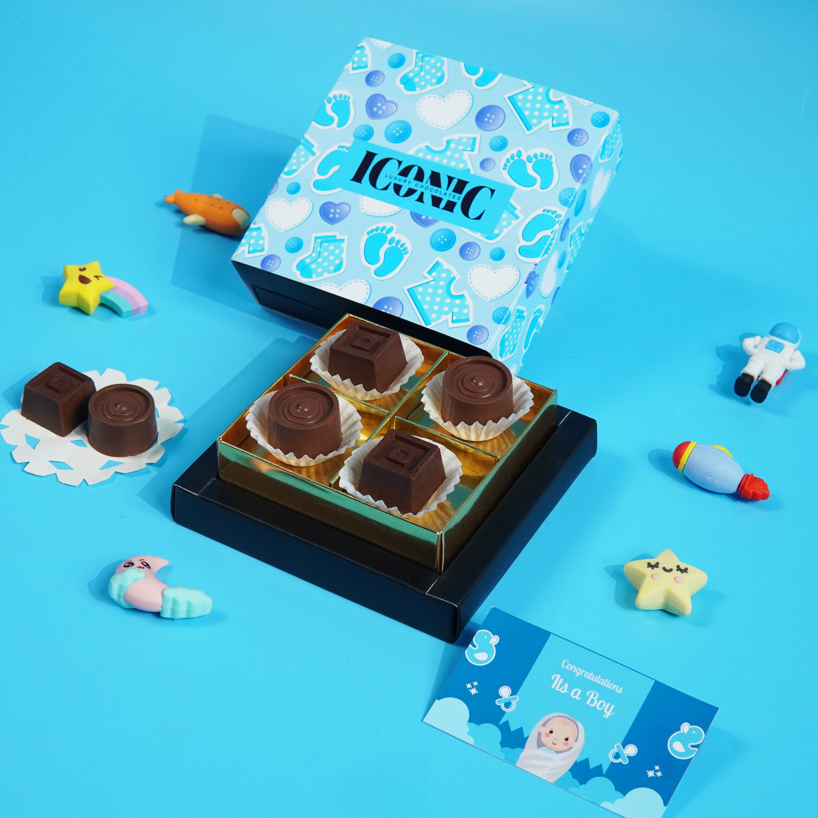 A blue baby-themed gift box with "ICONIC" branding, containing four handcrafted chocolate truffles, with a card that reads "Congratulations It's a Boy."