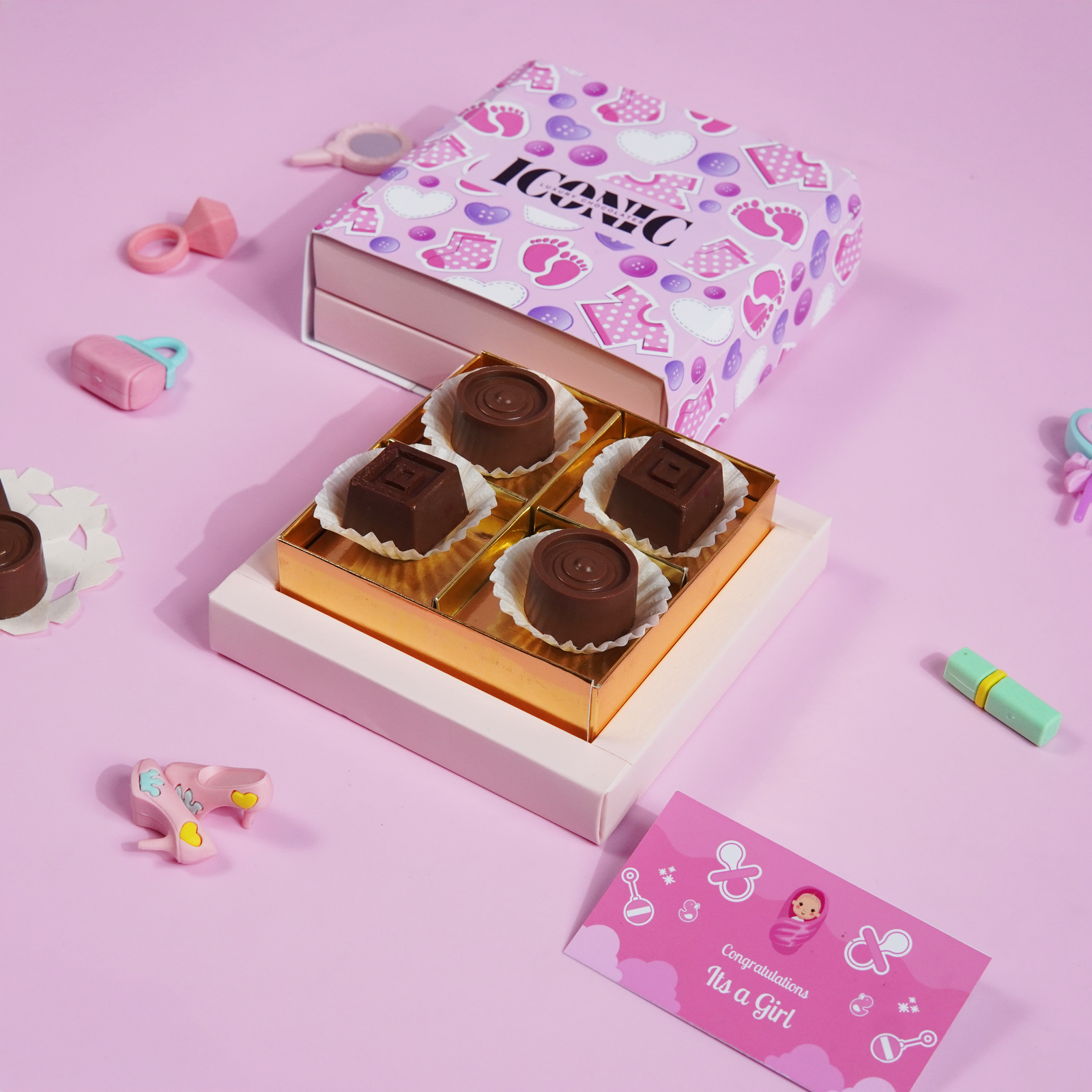 A pink baby-themed gift box with "ICONIC" branding, containing four handcrafted chocolate truffles, with a card that reads "Congratulations It's a Girl."