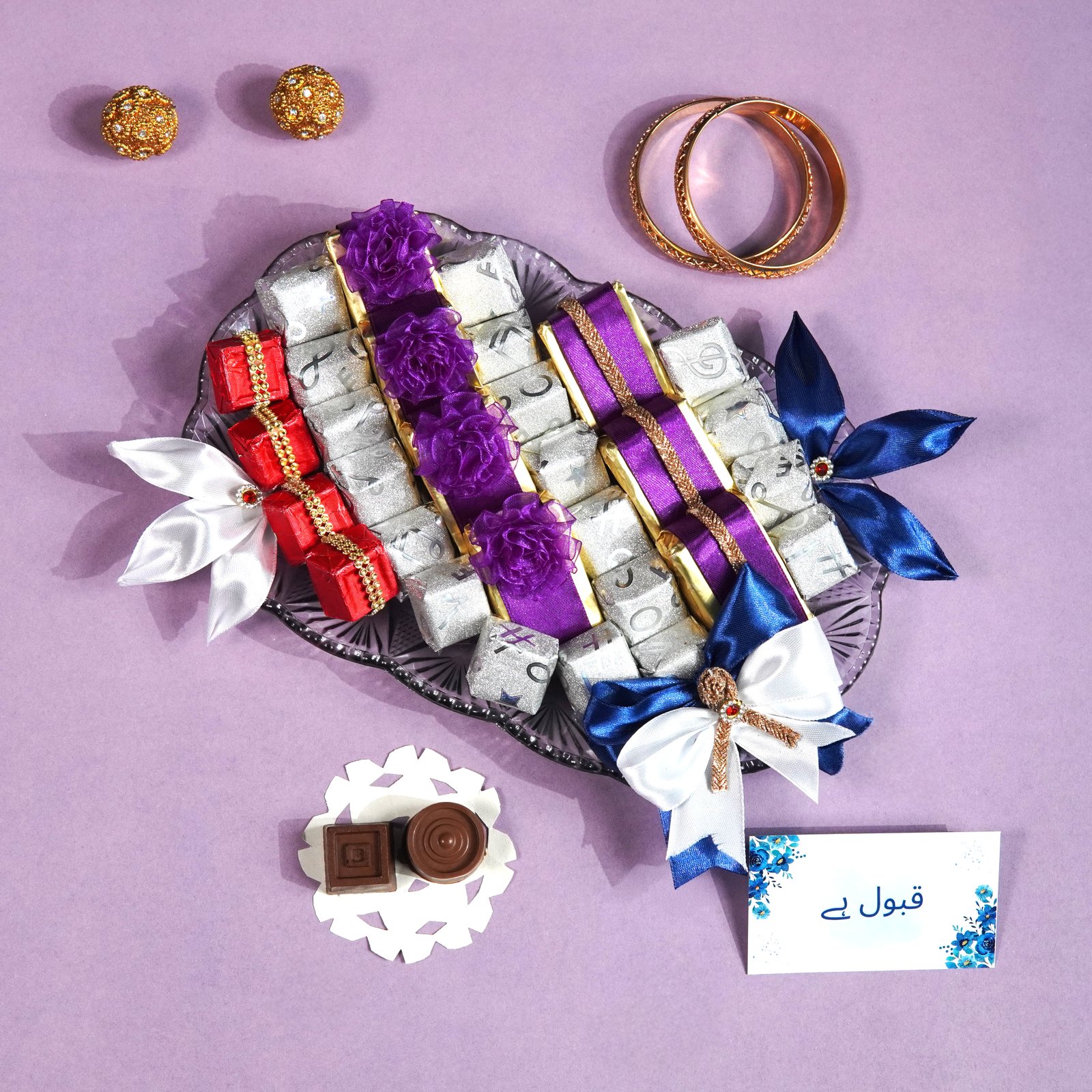 A glass platter filled with individually wrapped chocolate pieces in silver, red, and purple foil, decorated with silk ribbons and bows.