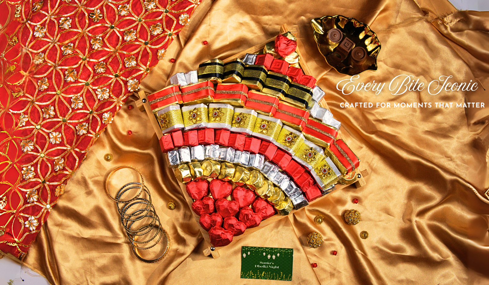 A golden silk banner with red and gold fabric, showcasing a large fan-shaped platter of individually wrapped chocolates in red, gold, and silver foil, with a "Happy Diwali" card.