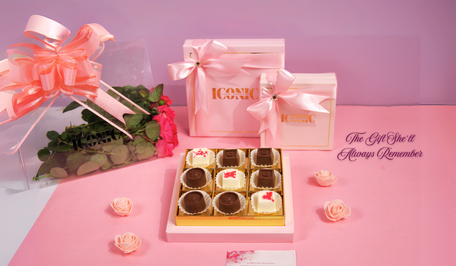 A pink and gold gift set with two boxes and a nine-piece chocolate tray, a bouquet of roses, and the phrase "The Gift She'll Always Remember."