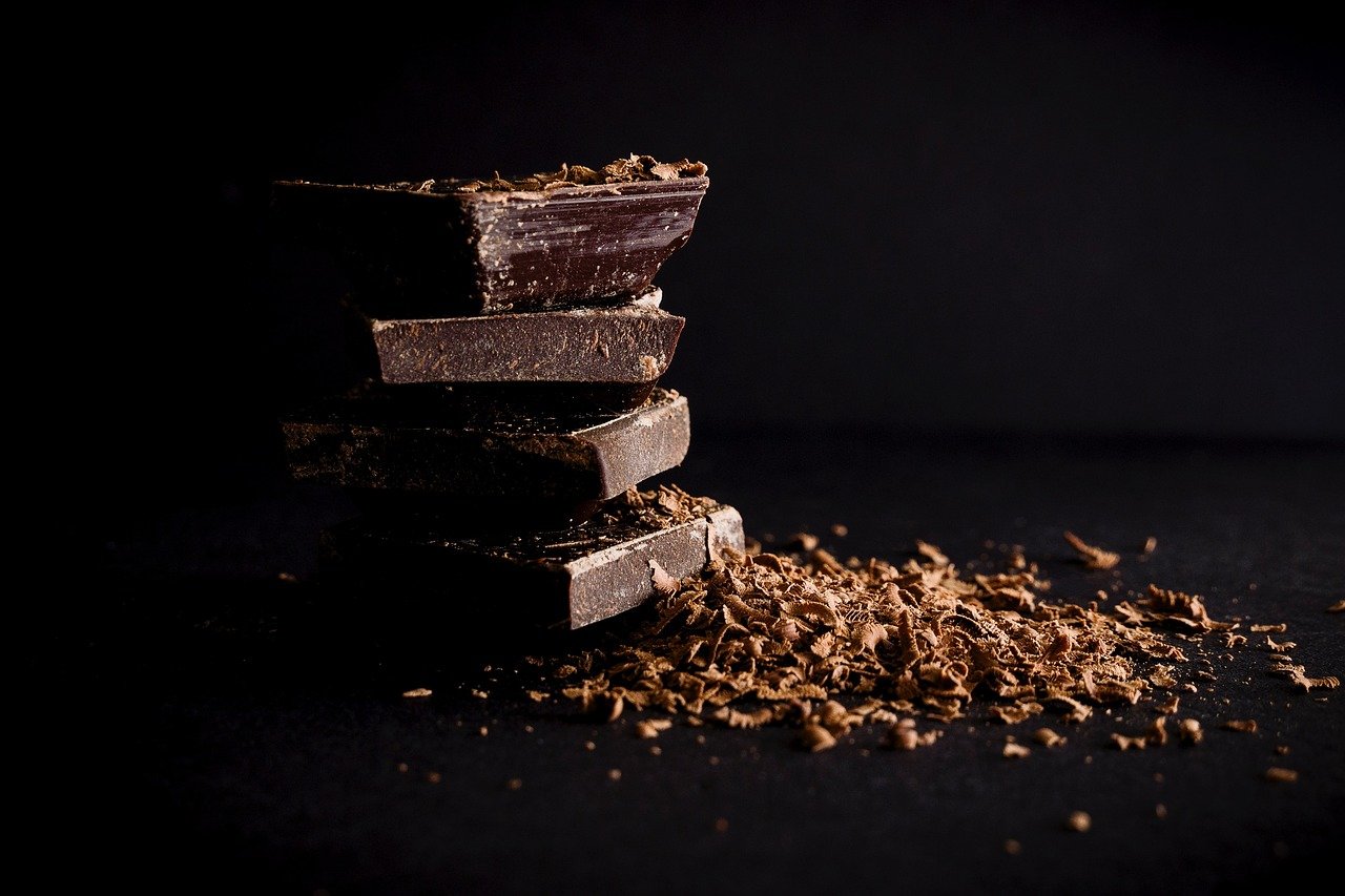 Stack of dark chocolate pieces with cocoa shavings on black background