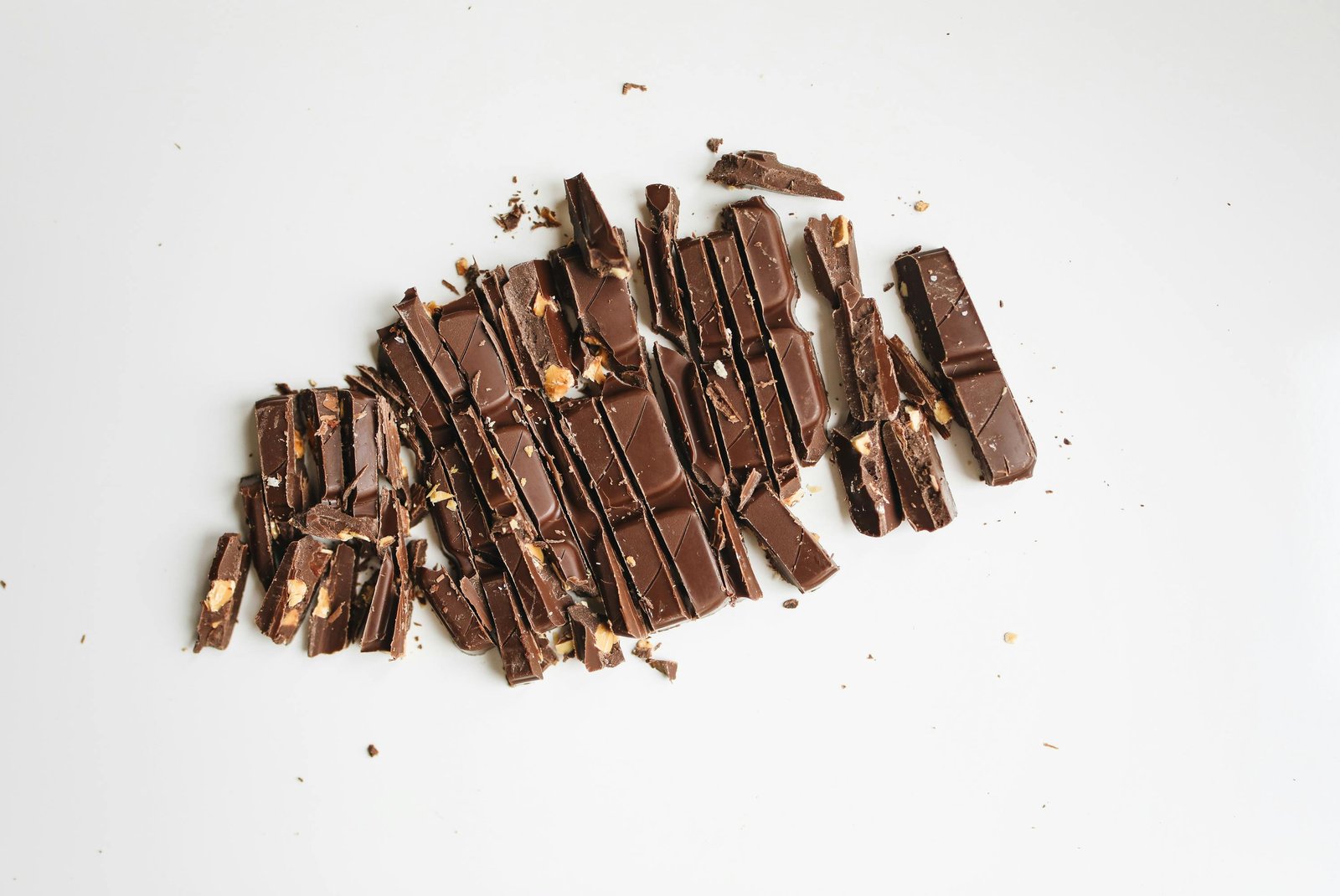 Broken pieces of milk chocolate with nuts on white background
