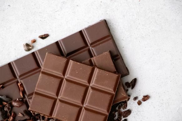 Dark chocolate squares with cocoa powder and cocoa beans on a rustic background.