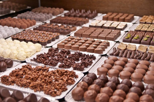 Assorted gourmet chocolates displayed on trays in a chocolate shop.