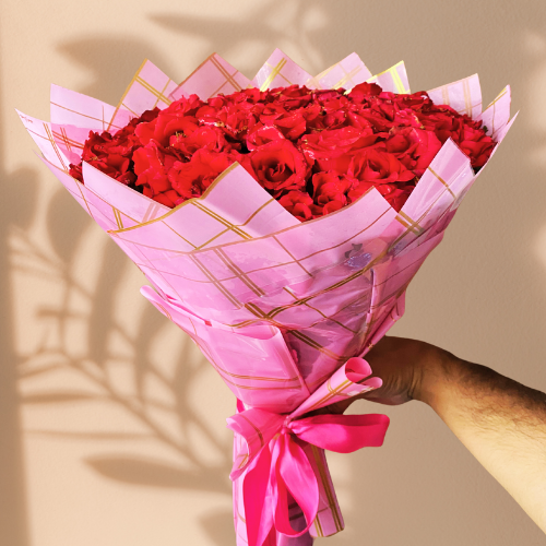 A beautiful bouquet of red roses, wrapped in pink and gold plaid paper.