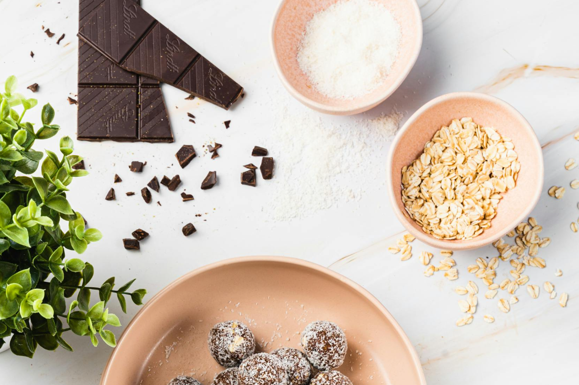 Dark chocolate bars with oats, coconut flakes, and healthy energy bites on a marble background.