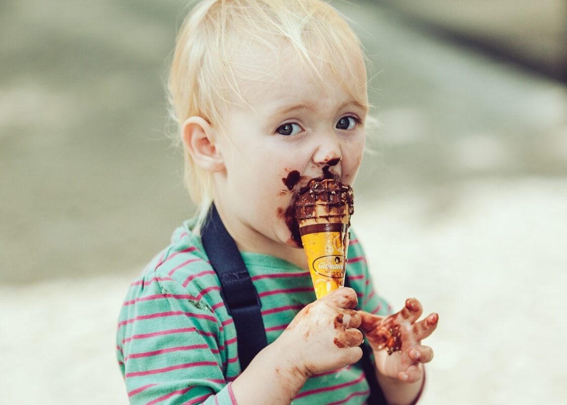 A young child with chocolate on face and hands eating an ice cream cone